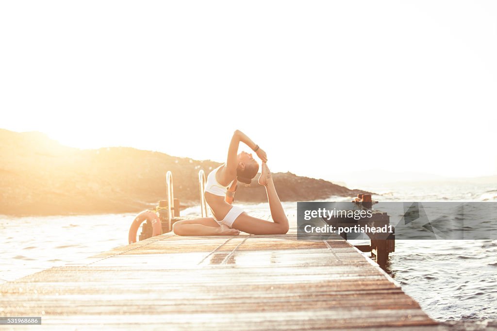 Young woman practices yoga on a pier