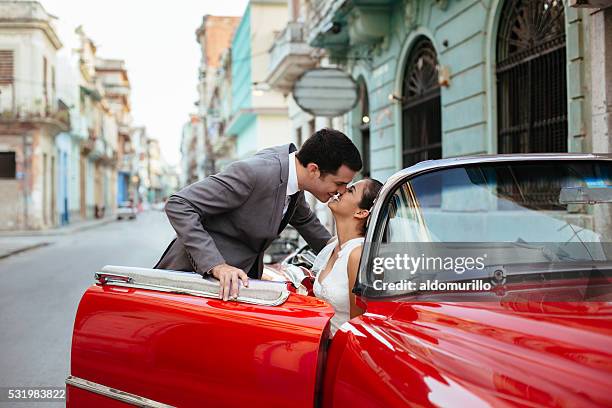 newlywed couple kissing in a red classic car - bride and groom wedding car stock pictures, royalty-free photos & images