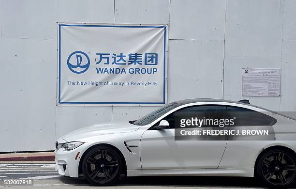 Driver in a BMW passes a Wanda Group banner on a construction site at 9900 Wilshire Boulevard in Beverly Hills, California, right beside the Beverly...