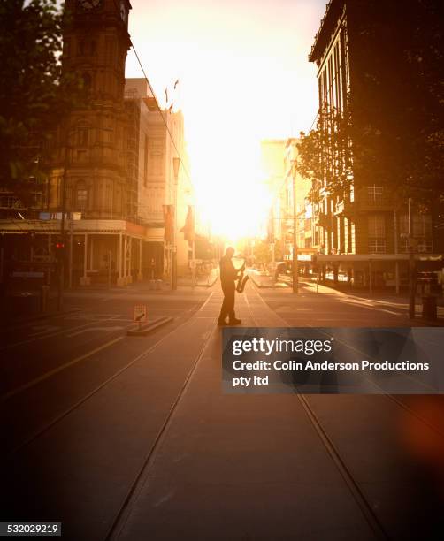 silhouette of caucasian musician holding saxophone on city street at sunrise - 大道芸人 ストックフォトと画像