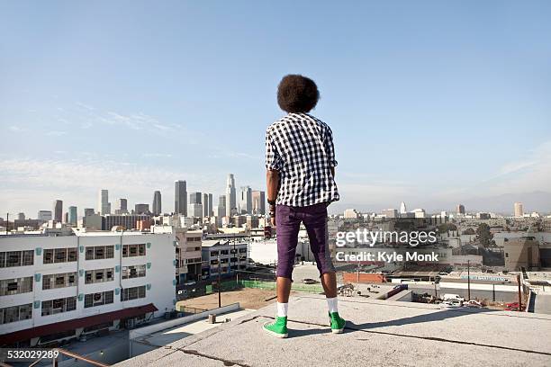 african american man overlooking cityscape from urban rooftop - trendy person stock-fotos und bilder