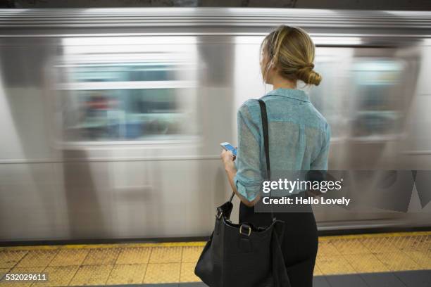 caucasian woman standing near passing subway in train station - new york personas fotografías e imágenes de stock