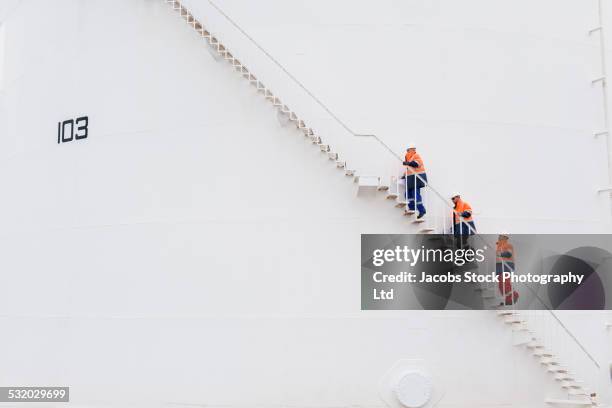 technicians climbing fuel storage tank staircase - sports helmet stock-fotos und bilder