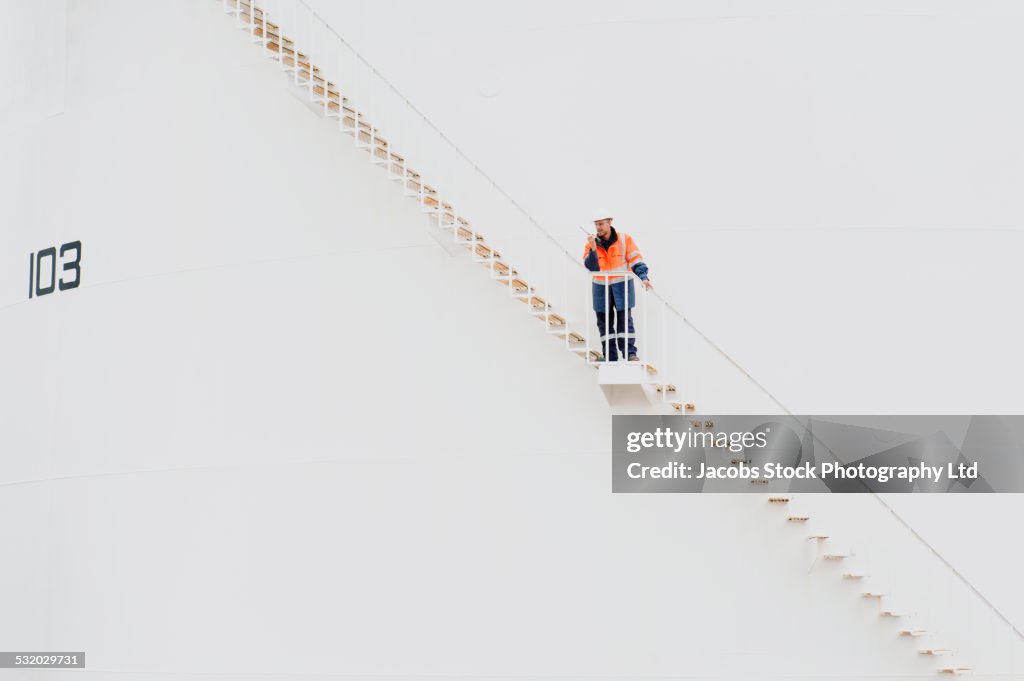 Caucasian technician using walkie-talkie on fuel storage tank staircase