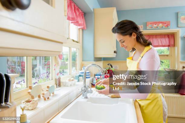 hispanic woman washing vegetables at kitchen sink - casalinga foto e immagini stock