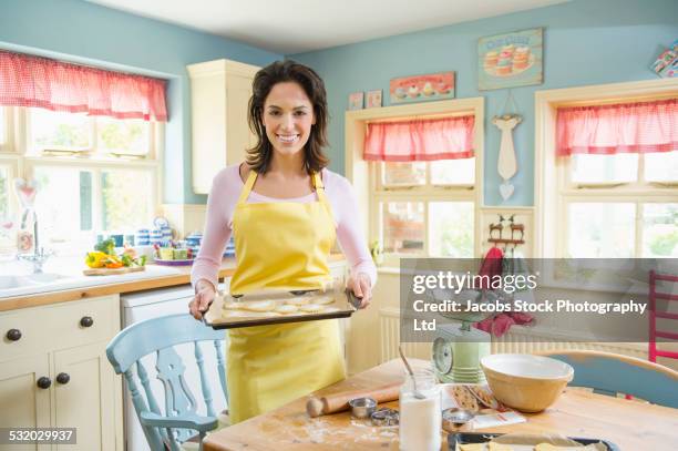 hispanic woman holding cookie sheet in kitchen - cookie sheet stock pictures, royalty-free photos & images