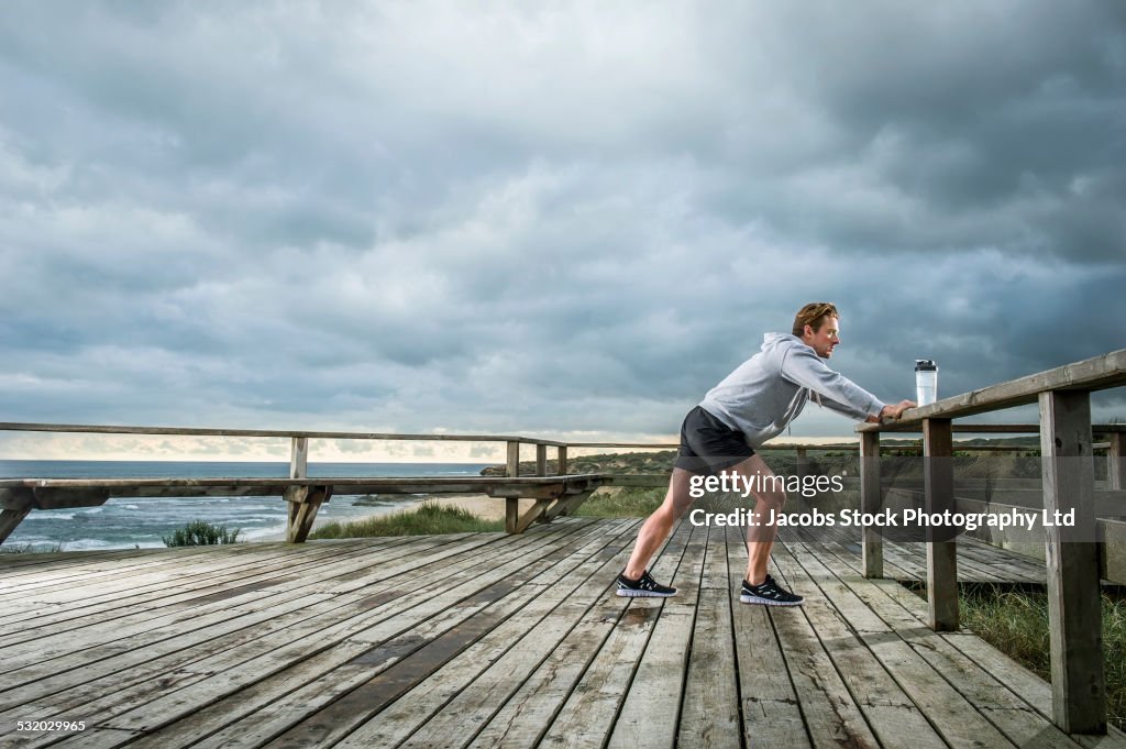 Caucasian runner stretching on wooden boardwalk at beach