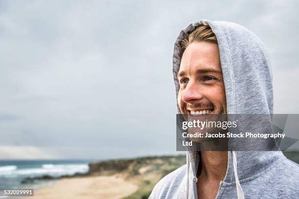 caucasian man smiling on beach - kapuze stock-fotos und bilder