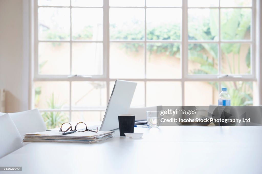 Laptop, paperwork and cup of coffee on dining room table