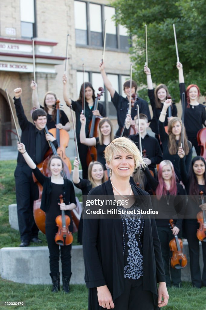 Student orchestra and teacher posing together outside high school