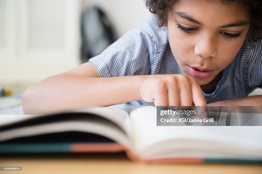 Mixed race boy reading book at desk