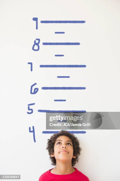 mixed race boy measuring his height on wall chart - child's wall height stock-fotos und bilder