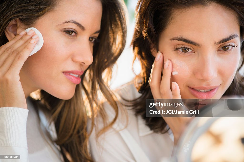 Hispanic women applying makeup in mirror