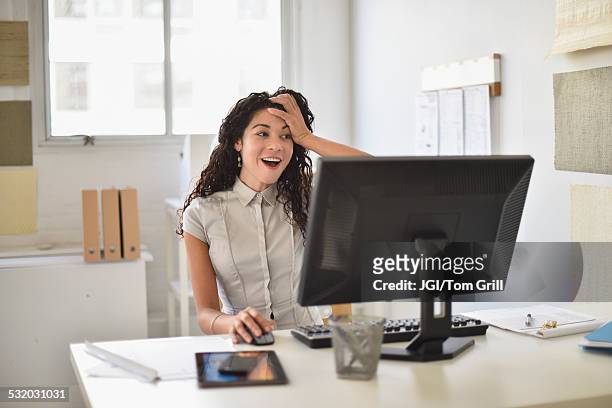 mixed race businesswoman gasping at computer at desk in office - surprised woman looking at tablet stock pictures, royalty-free photos & images