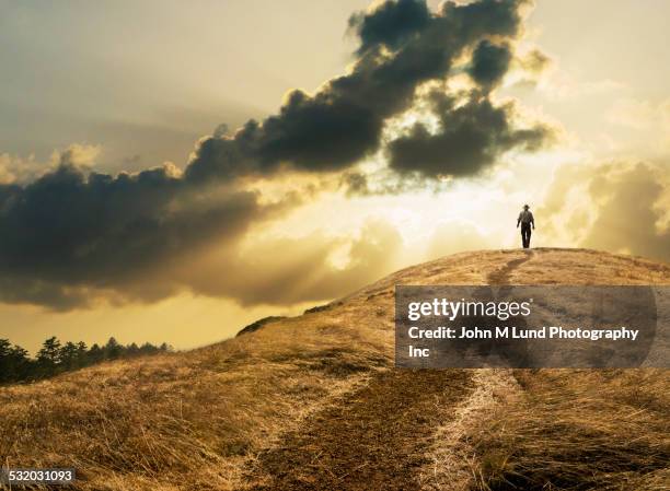 man walking under dramatic clouds over grassy rural hill - distant hills stock pictures, royalty-free photos & images