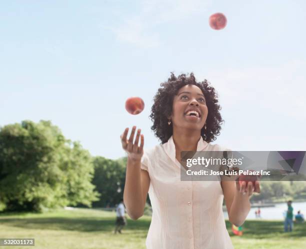 african american woman juggling fruit in park - juggler stock-fotos und bilder