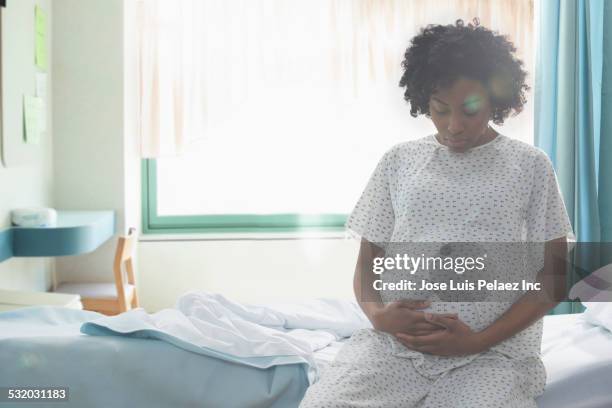 pregnant african american woman holding her stomach in hospital - pregnant women stock-fotos und bilder