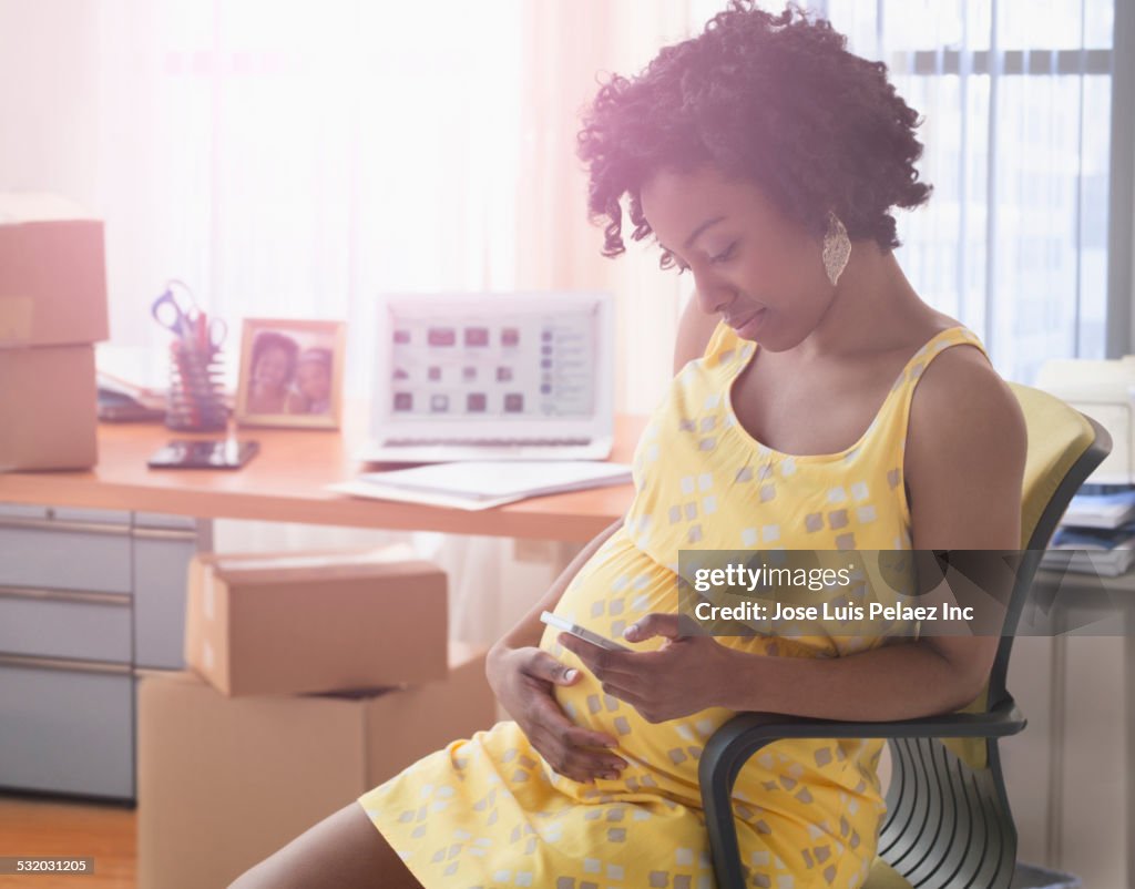 Pregnant African American businesswoman holding her stomach in office with boxes