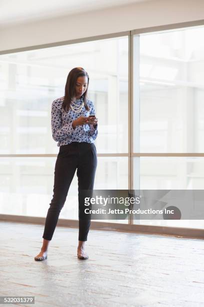 african american businesswoman using cell phone in office lobby - receiving fotografías e imágenes de stock
