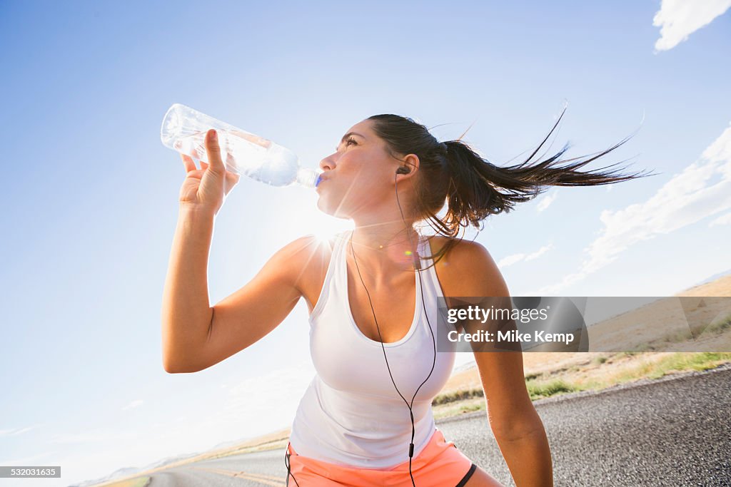 Caucasian runner drinking water bottle on remote road