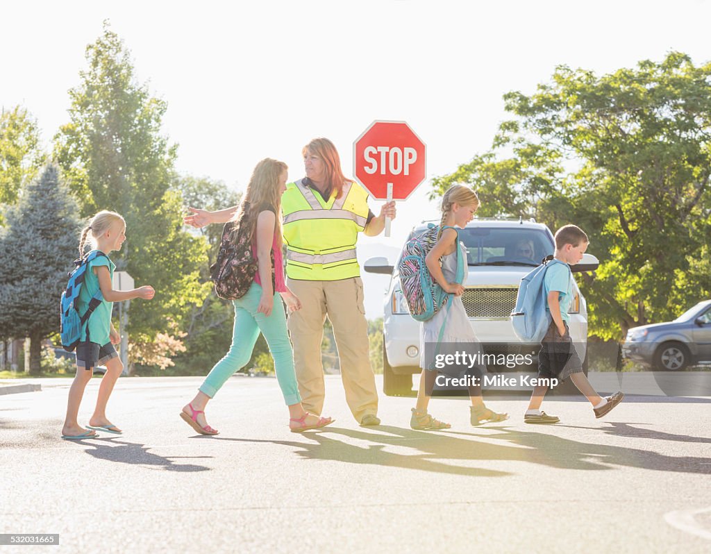Caucasian crossing guard helping children in crosswalk