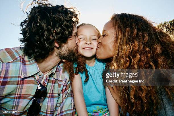 Parents kissing cheeks of daughter outdoors