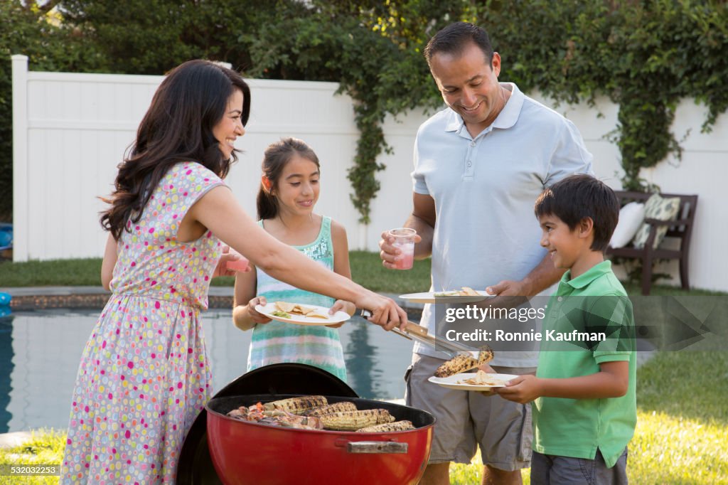 Hispanic mother serving family at backyard barbecue