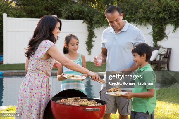 hispanic mother serving family at backyard barbecue - couple grilling stock pictures, royalty-free photos & images