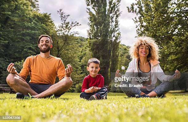 jeune famille heureuse faisant du yoga exercices de détente sur une herbe. - family yoga photos et images de collection