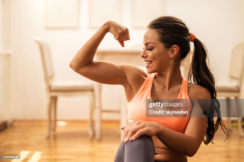 Happy athletic woman flexing her bicep at home.