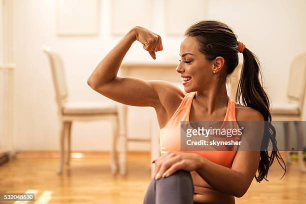 happy athletic woman flexing her bicep at home. - strength stock pictures, royalty-free photos & images