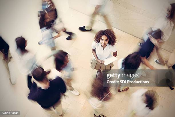 nervous student standing still in busy private school hallway - african american school uniform stock pictures, royalty-free photos & images