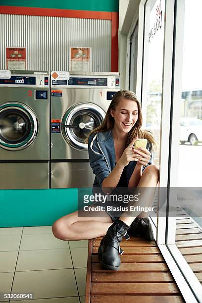 young woman in laundromat - wäscherei stock-fotos und bilder