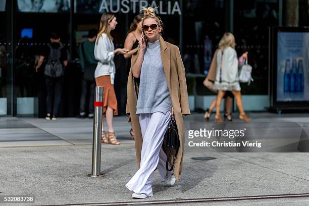 Guest wearing an oversized brown coat, a grey sweater and wide white pants outside C Meo Collective at Mercedes-Benz Fashion Week Resort 17...