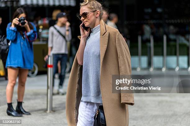 Guest wearing an oversized brown coat, a grey sweater and wide white pants outside C Meo Collective at Mercedes-Benz Fashion Week Resort 17...