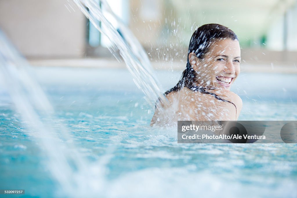 Woman relaxing under fountain in swimming pool