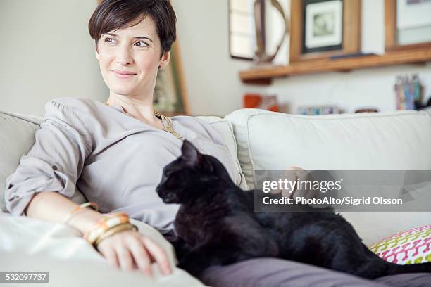 woman relaxing on sofa with cat on her lap - bachelorette photos et images de collection