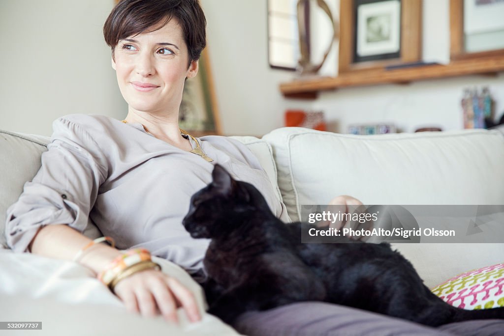 Woman relaxing on sofa with cat on her lap