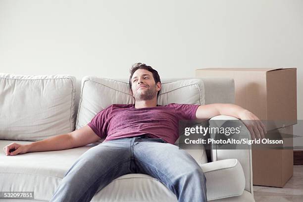 man relaxing on sofa while moving house - recostarse fotografías e imágenes de stock