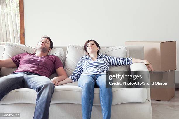 couple relaxing on sofa while moving house - tired couple stock pictures, royalty-free photos & images