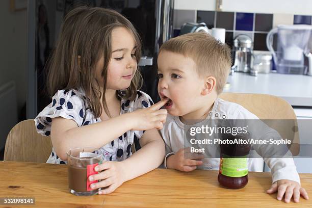 young siblings tasting contents of jars with their fingers - sisters feeding stock pictures, royalty-free photos & images