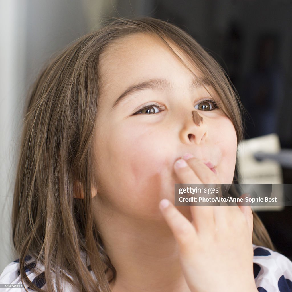 Girl with chocolate smeared on her nose, licking fingers