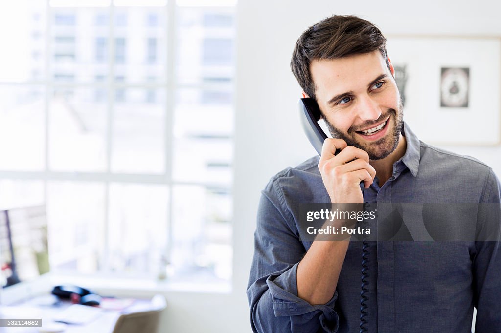Happy businessman using landline phone in office