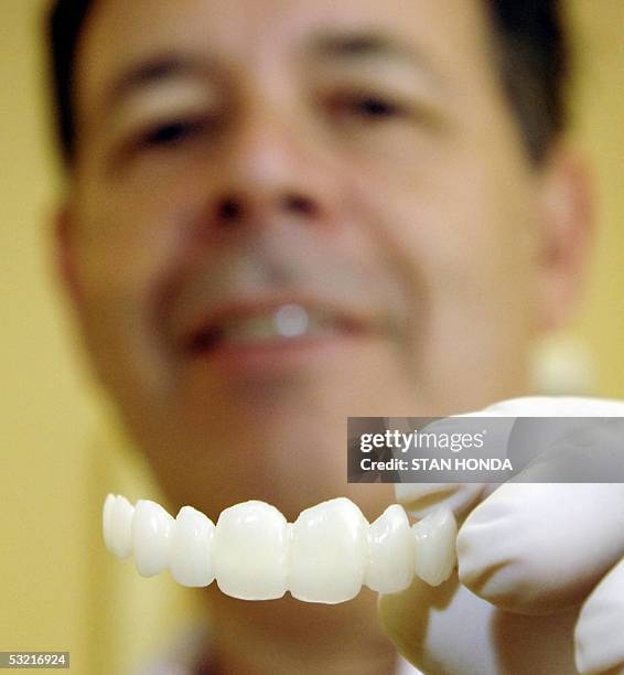 New York, UNITED STATES: TO GO WITH AFP STORY "USA-SOCIETE-BEAUTE" BY CATHERINE HOURS Dentist Jeff Golub-Evans holds a prosthetic row of teeth made...