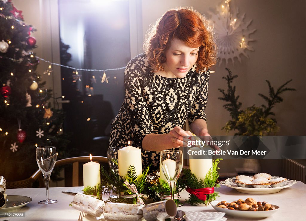 Woman lights candles on Christmas dining table.