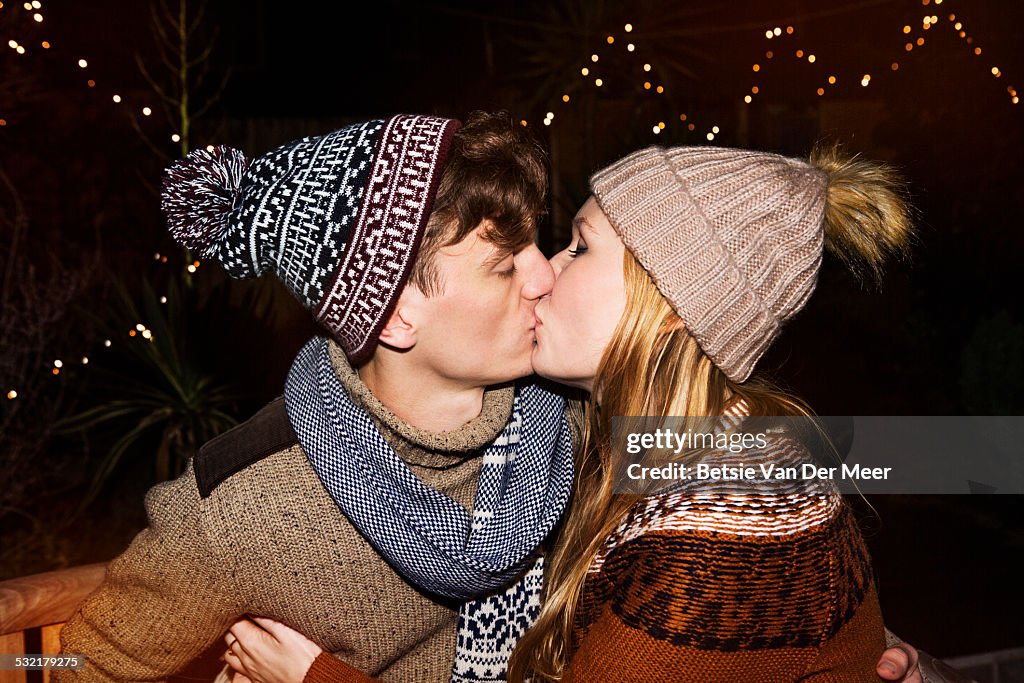 Couple kissing, surrounded by outdoor lights.