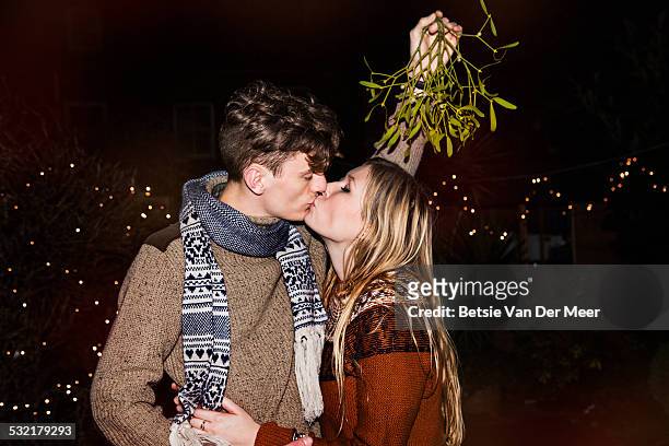 couple kissing outdoors under mistletoe - christmas couple stockfoto's en -beelden