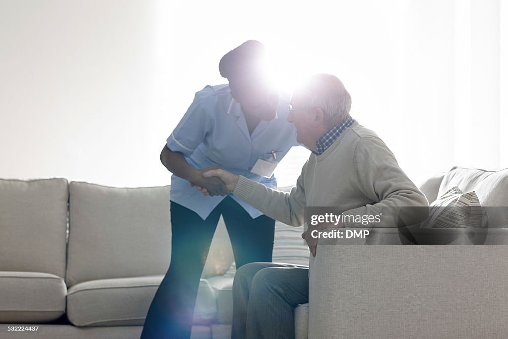 Female caregiver helping senior man get up from sofa