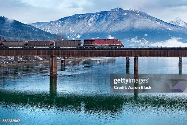red train on bridge above river in mountains - cargo train stock pictures, royalty-free photos & images