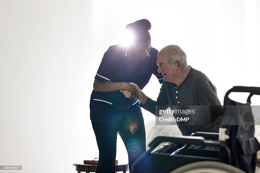 Female nurse helping senior man get up from bed